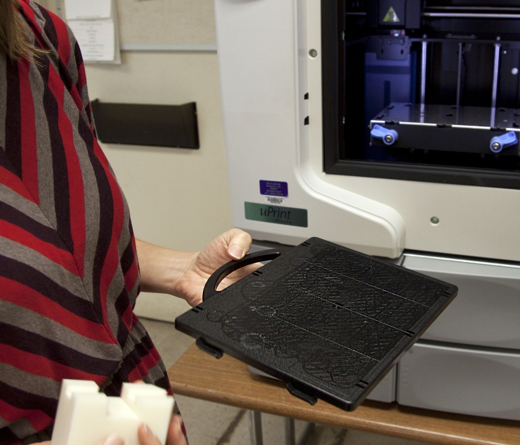 Professor Elizabeth Cheung (not pictured) holding a plastic tray, explains the function of a part of Pierce College's 3D printer. She says that this is where the ink deposits on. Photo: Lisa Richardson