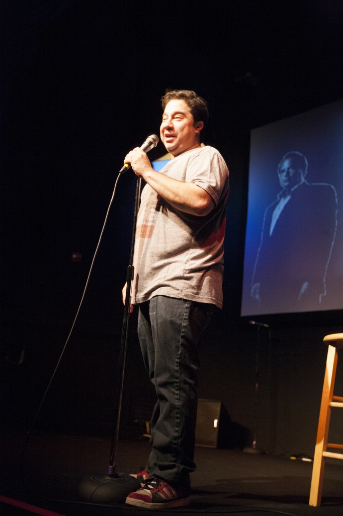 At the Jon Lovitz Comedy Club, Greg Wilson eases into his routine as the projected image of Lovitz gazes into the future of comedy. Photo: Mohammad Djauhari