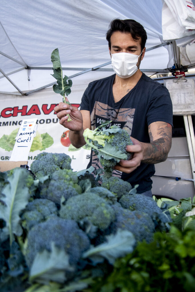 Carlos Chaves places brocoli on the C. Chavez farm stand at the Encino Farmers Market in Van Nuys, Calif., on April 4, 2020. Photo by Katya Castillo.